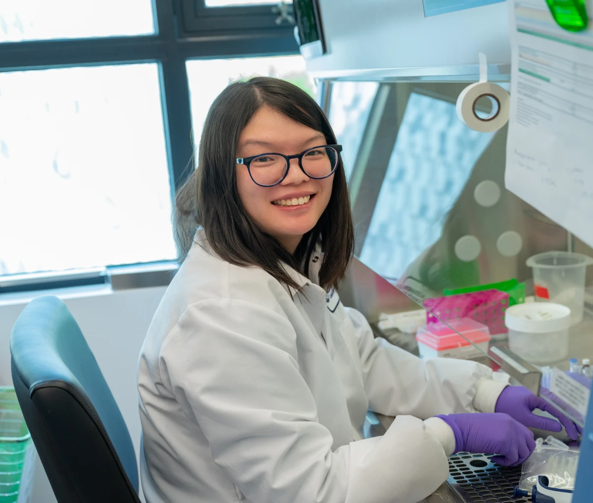 Scientist wearing a white lab coat and purple gloves surrounded by lab equipment